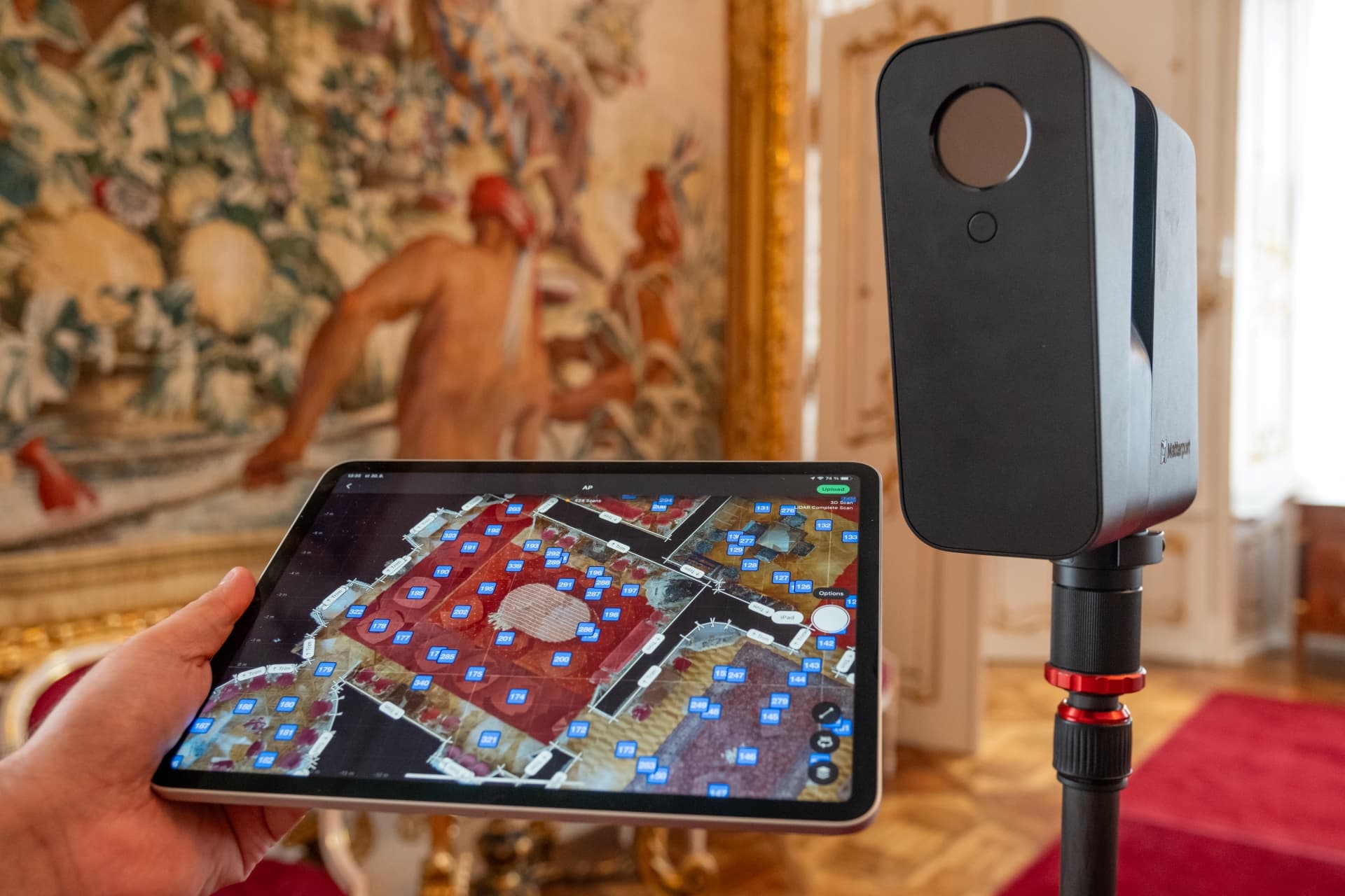 Ruka drží tablet v prostoru Arcibiskupského paláce. Na stativu stojí 3D skener